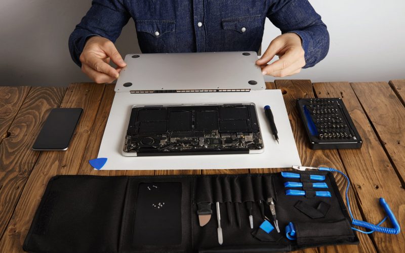 service-man-opens-backside-topcase-cover-of-computer-laptop-before-repairing-cleaning-and-fixing-it-with-his-professional-tools-from-toolkit-box-near-on-wooden-table-front-view (1)